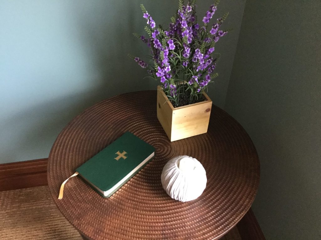 A small table with a bible, flowers and a small ball sitting on it.
